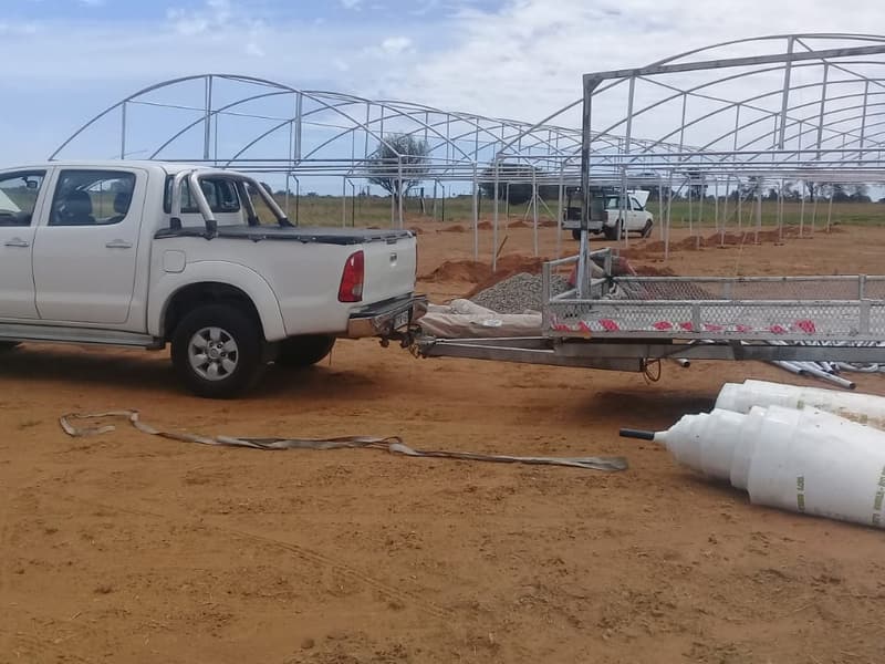 Rolls of tunnel plastic beside a trailer, with tunnel frames going up behind