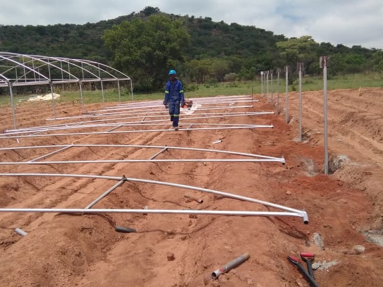 Steel arches laid out on ridged soil next to a line of posts set in concrete