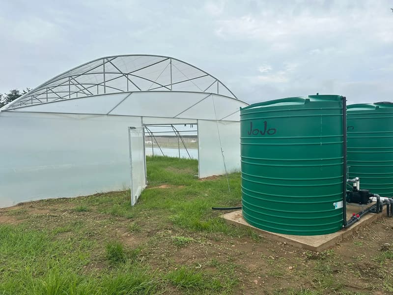 Two green JoJo tanks with a pump and valves on a concrete slab beside a tunnel